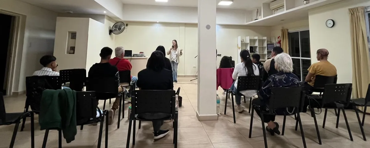 Vista panorámica del salón con una oradora al frente y la comunidad sentada